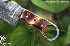 Burnt bone handle of the Damascus steel gut hook knife, featuring a comfortable grip and finger hole for enhanced control during use.