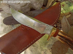Handmade hunting knife with a drop point blade, brass hilt, stag antler handle, and brown leather sheath.