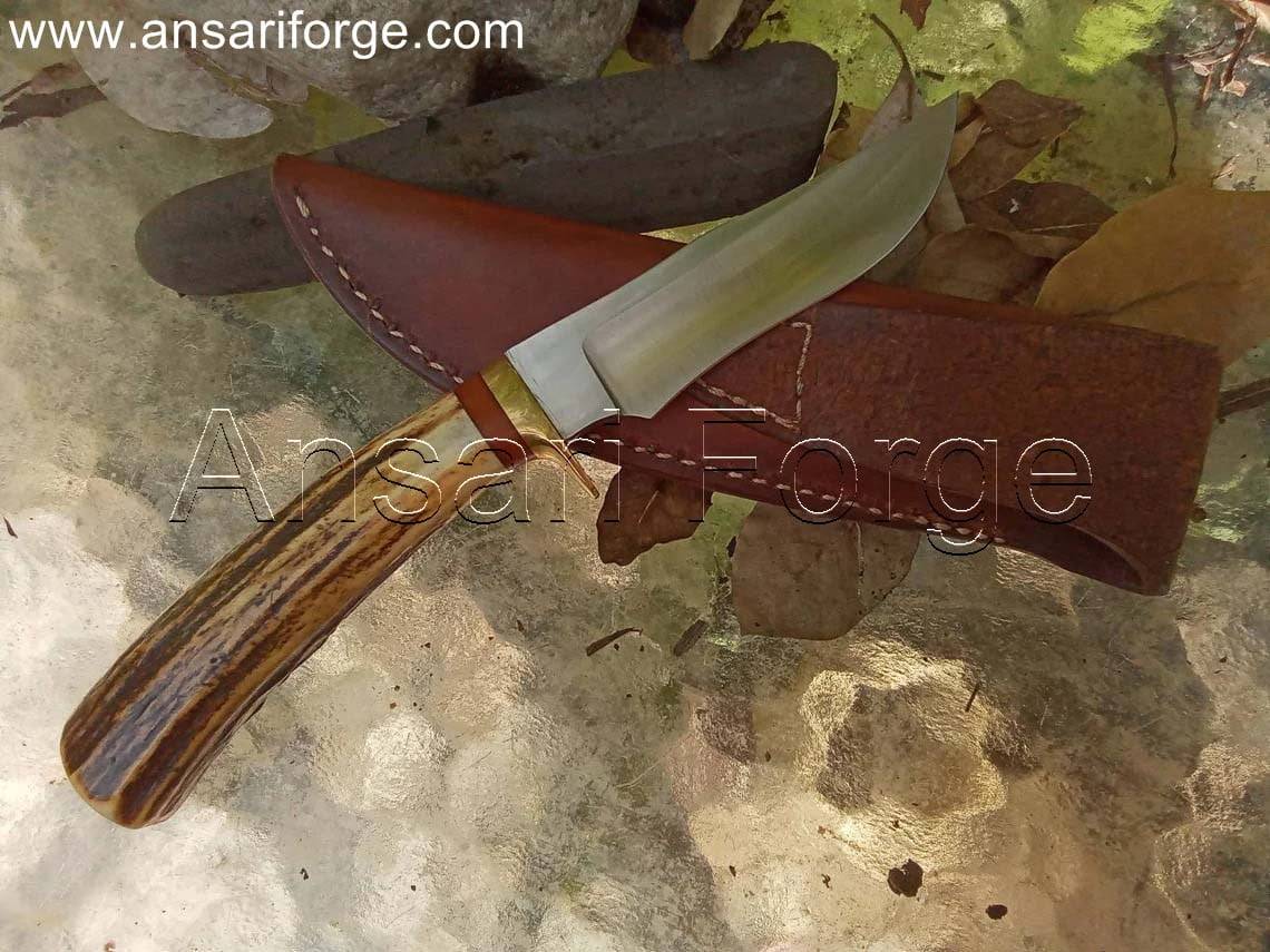 Handmade hunting knife with a drop point blade, brass hilt, stag antler handle, and brown leather sheath.