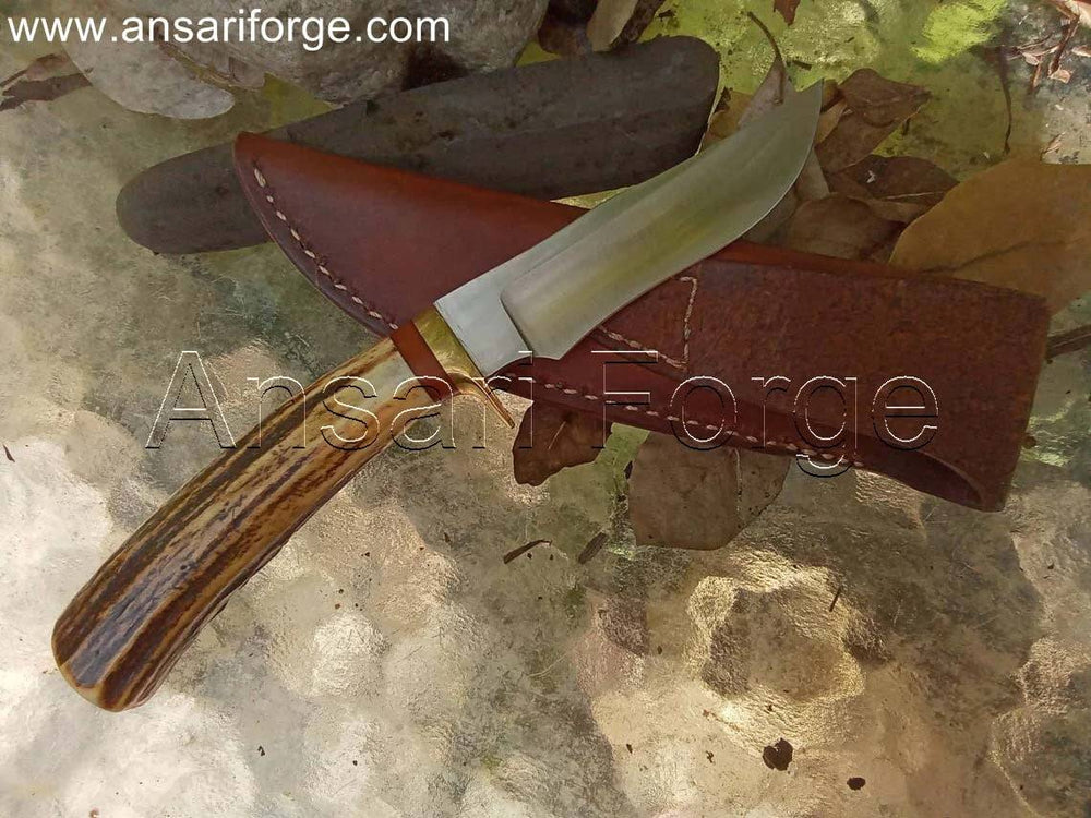 Handmade hunting knife with a drop point blade, brass hilt, stag antler handle, and brown leather sheath.