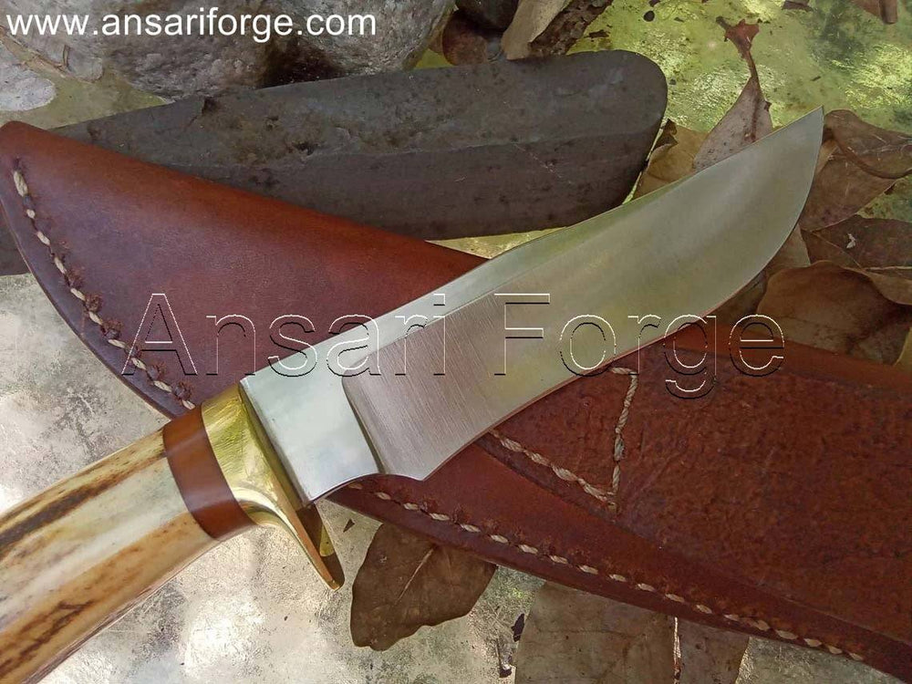 Handmade hunting knife with a drop point blade, brass hilt, stag antler handle, and brown leather sheath.