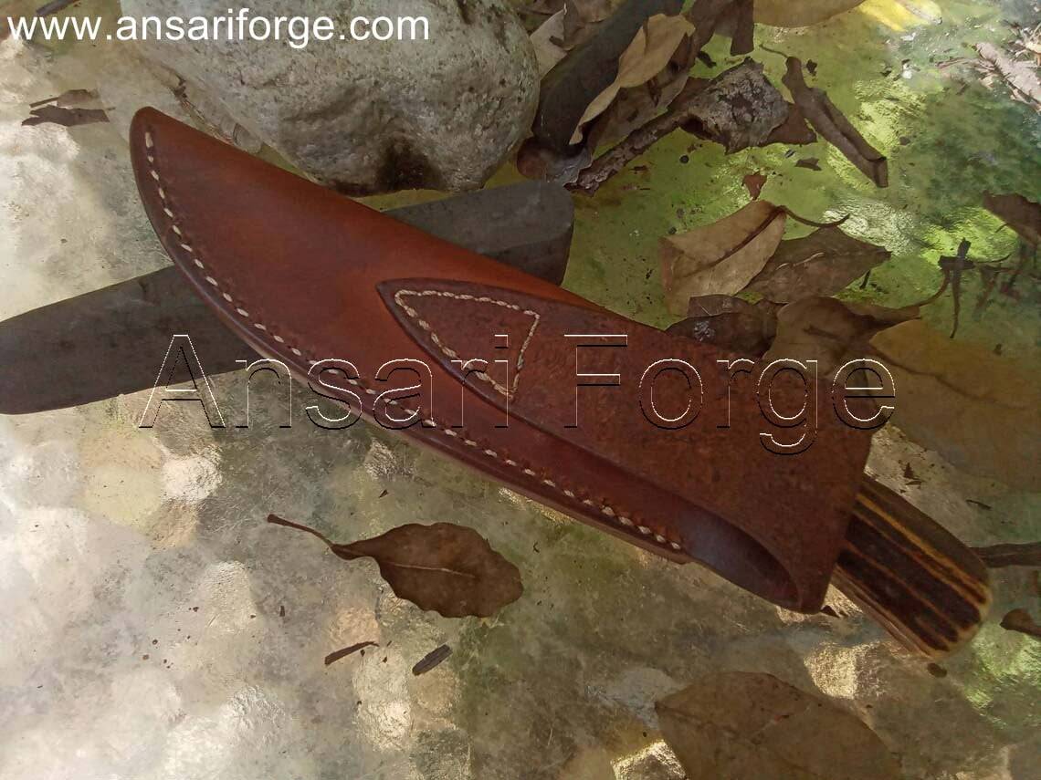 Handcrafted hunting knife with drop point blade, stag antler handle, and leather sheath.