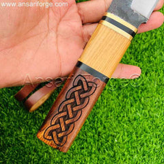 A close-up of the Beagnoth seax knife's handle, showcasing the intricate Norse carvings and the brass bolsters.