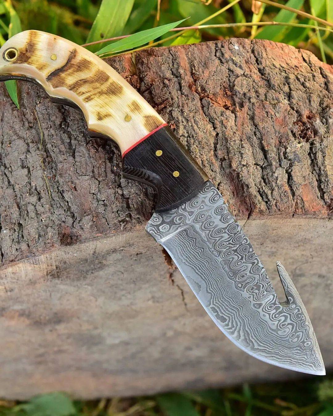 Damascus skinning knife with gut hook, leather sheath, and sheep horn handle.High-quality hunting knife with comfortable grip and sharp blade.
