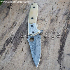 Close-up of Custom Damascus Folding Pocket Knife. Rain drop pattern Damascus steel blade open, revealing engraved brass bolsters and bone handle. Leather pouch sits beside the knife.